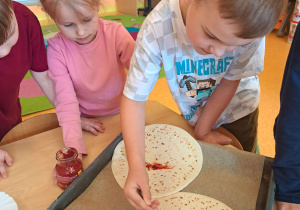 Dzieci dekorują pizzę.
