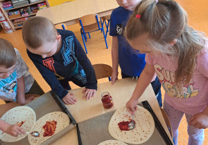 Dzieci dekorują pizzę.