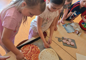 Dzieci dekorują pizzę.
