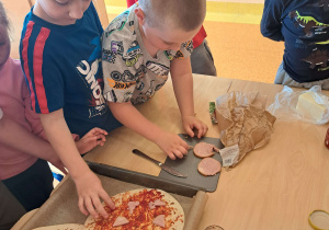 Dzieci dekorują pizzę.