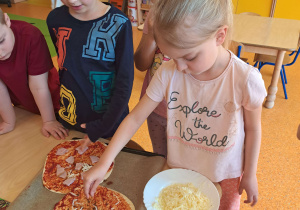 Dzieci dekorują pizzę.