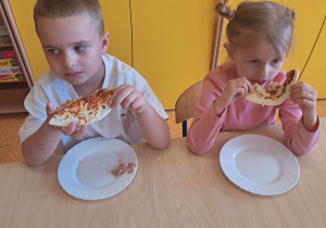 Dzieci konsumują wykonaną pizzę.