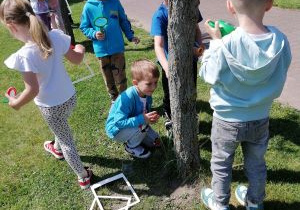 Dzieci obserwują owady w ogrodzie przedszkolnym z wykorzystaniem narzędzi badawczych.