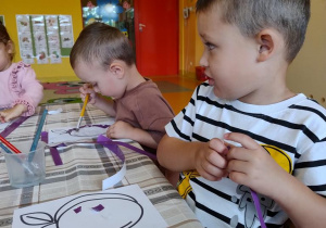 Dzieci wyklejają szablon śliwki wydzierankami.