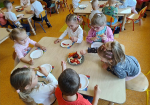 Dzieci wybierają kawałki różnych owoców oraz warzyw i nakładają je na talerze.