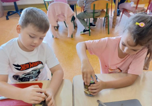 Dzieci wkładają owoce do słoików.