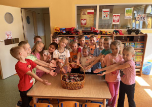 Dziecie stoją wokół stolika na którym leży koszyk z przetworami.