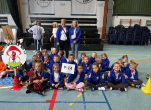 Dzieci siedzą na podłodze, obok stoi logo przedszkola.