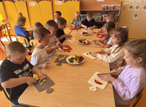 Dzieci kroją nożem owoce na deseczkach.