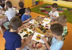 Dzieci naklejają liście na kartkę.