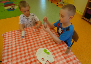Dwóch chłopców maluje zieloną farbą rolki od papieru