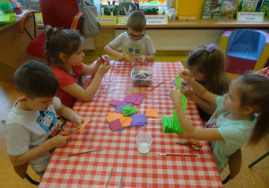 Pięcioro dzieci siedzi przy stole i wykonują elementy do makiety