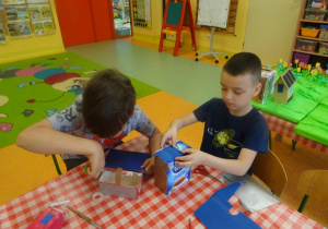 Dwóch chłopców owija pudełka kolorowymi wycinankami