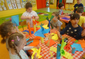 Pięć dziewczynek siedzi przy stoliku i wykonują wiatraki z rolek i kolorowego papieru