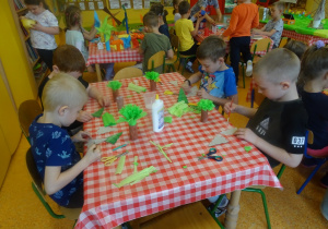 Dzieci siedzą przy stolikach i wykonują elementy do makiety