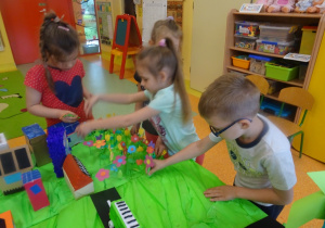 Troje dzieci układa na makiecie kwiaty