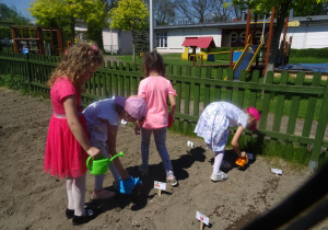 Cztery dziewczynki trzymają konewki i podlewają w ogródku