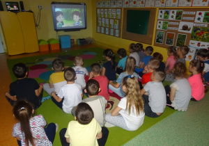 Dzieci siedzą na dywanie i oglądają film edukacyjny