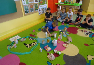 Dzieci siedzą na dywanie, jeden chłopiec siedzi w środku i wybiera produkty ekologiczne