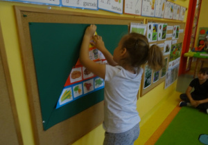 Dziewczynka przypina do tablicy jeden z elementów piramidy zdrowia