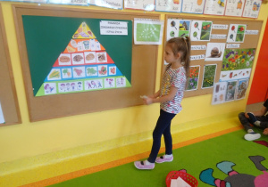 Dziewczynka stoi przed tablicą i dopina brakujący element do piramidy zdrowia