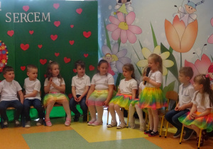 Dzieci siedzą w w półkolu, Gabrysia stoi, trzyma mikrofon, mówi wiersz