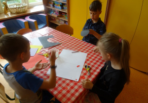 Troje dzieci siedzi przy stoliku i wykonują prace plastyczne