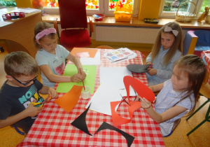 Czwórka dzieci siedzi przy stoliku i wykonują prace plastyczne