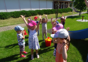 Dzieci zebrały piłeczki do kosza i podnoszą ręce do góry