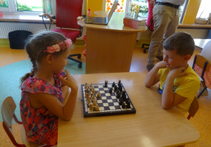 Natalka i Filip grają w szachy, siedzą na przeciwko siebie