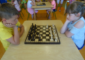 Filip i Amelka siedzą na przeciwko siebie i grają w szachy
