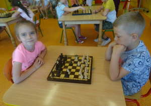 Kaja i Krzysiu siedzą na przeciwko siebie i grają w szachy