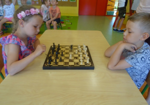 Natalka i Krzysiu siedzą na przeciwko siebie i grają w szachy