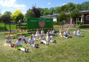 Dzieci siedzą w siadzie prostym na trawie