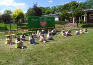 Dzieci siedzą w siadzie skulnym na trawie