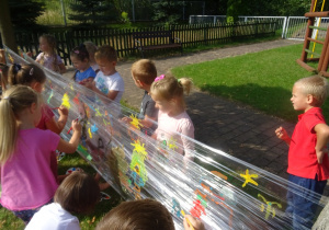 Dzieci malują na folii rozłożonej pomiędzy pniami drzew.