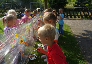 Dzieci malują na folii rozłożonej pomiędzy pniami drzew.