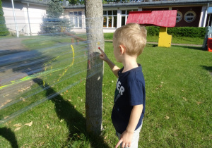 Chłopiec maluje paluszkami na foli rozłożonej pomiędzy drzewami.