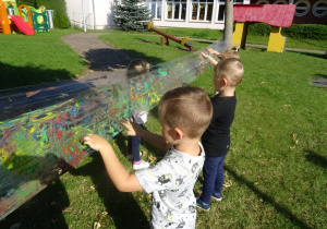 Dwóch chłopców maluje paluszkami na foli rozłożonej pomiędzy drzewami.