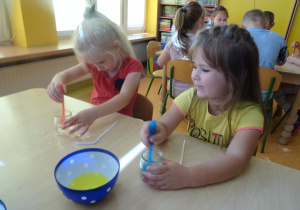 Dzieci mieszają słomką wodę z płynem.