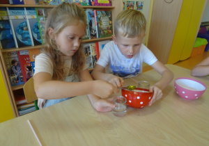 Dzieci nalewają łyżkami płyn do słoiczków z wodą.