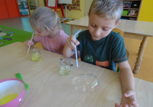 Dzieci nalewają łyżkami płyn do słoiczków z wodą.