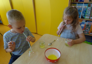 Dzieci robią bańki mydlane, dmuchają przez słomkę.