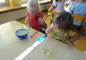 Dzieci robią bańki mydlane, dmuchają przez słomkę.