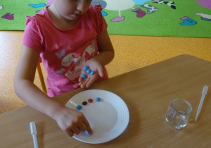 Dziewczynka układa na talerzu kolorowe cukierki.