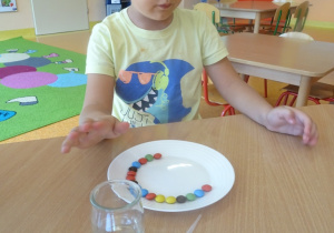 Chłopiec układa na talerzu kolorowe cukierki