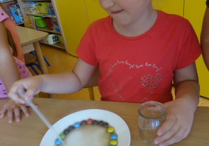 Dziewczynka nalewa wodę pipetą na talerz.