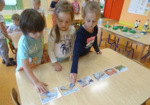 Trójka dzieci układa wspólnie historyjkę obrazkową.