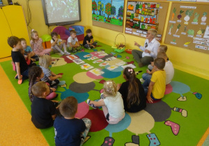 Dzieci siedzą wokół ilustracji owoców.