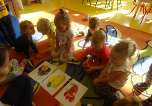 Grupa dzieci siedzi wokół ilustracji z owocami.